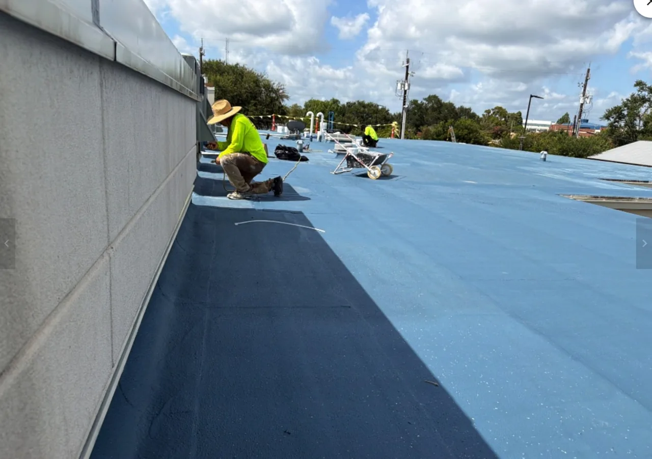 Ramtech crew applying a fluid-applied base coat along a parapet wall on a low-slope roof