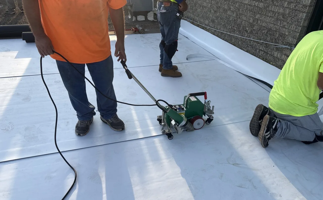 Roofer heat-welding a TPO membrane repair with a hot-air welder