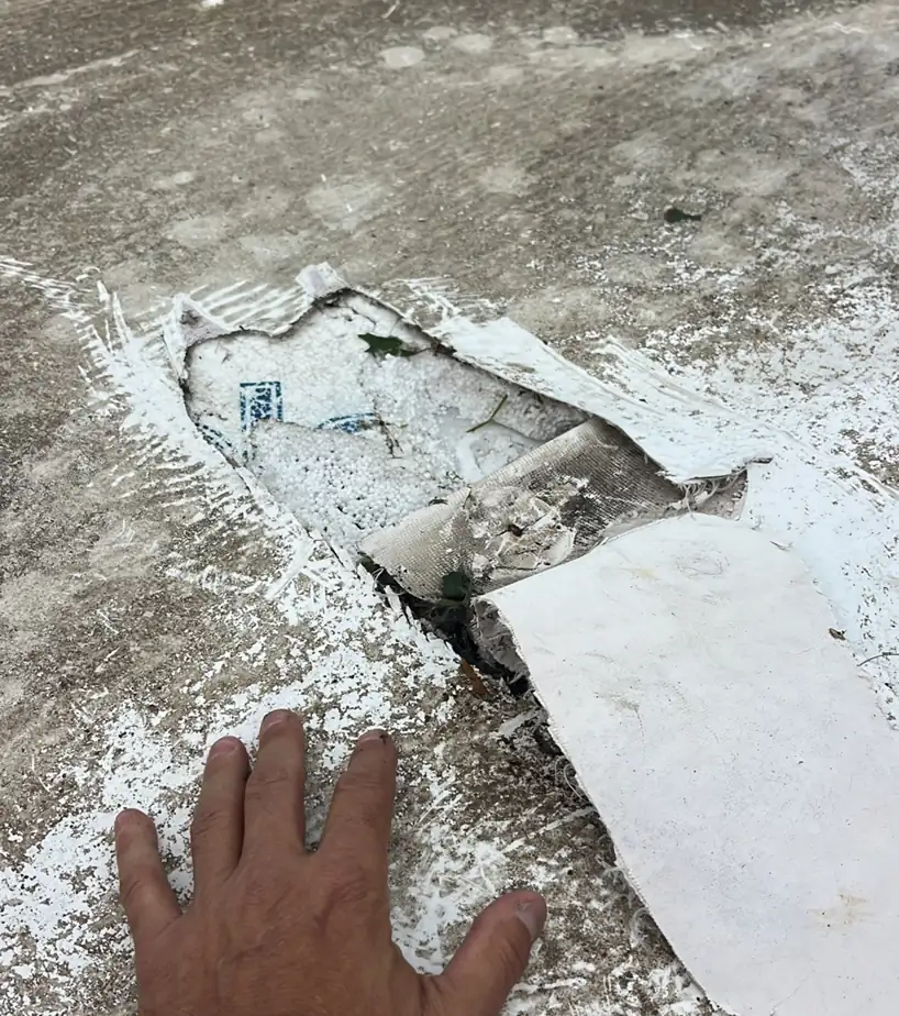 Section of TPO roof membrane cut out by Ramtech during a blister repair next to a rooftop blower, with a hand for scale