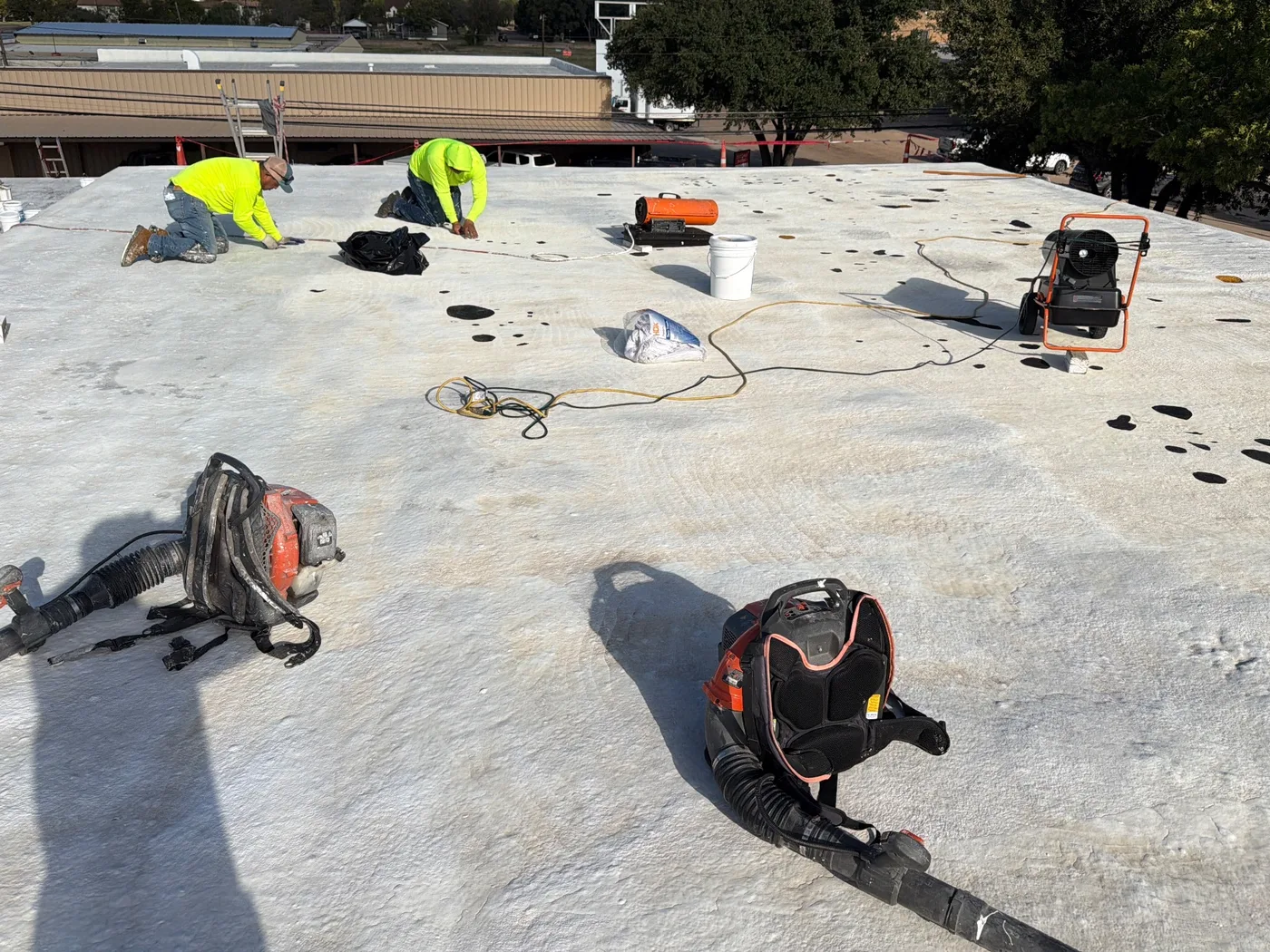 Roofing crew working on knees across a low-slope roof with blowers and equipment in Ballinger, Texas