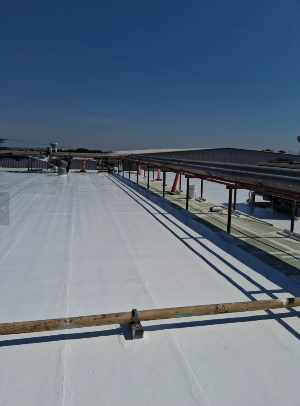 Long run of restored white roof along a rooftop pipe line