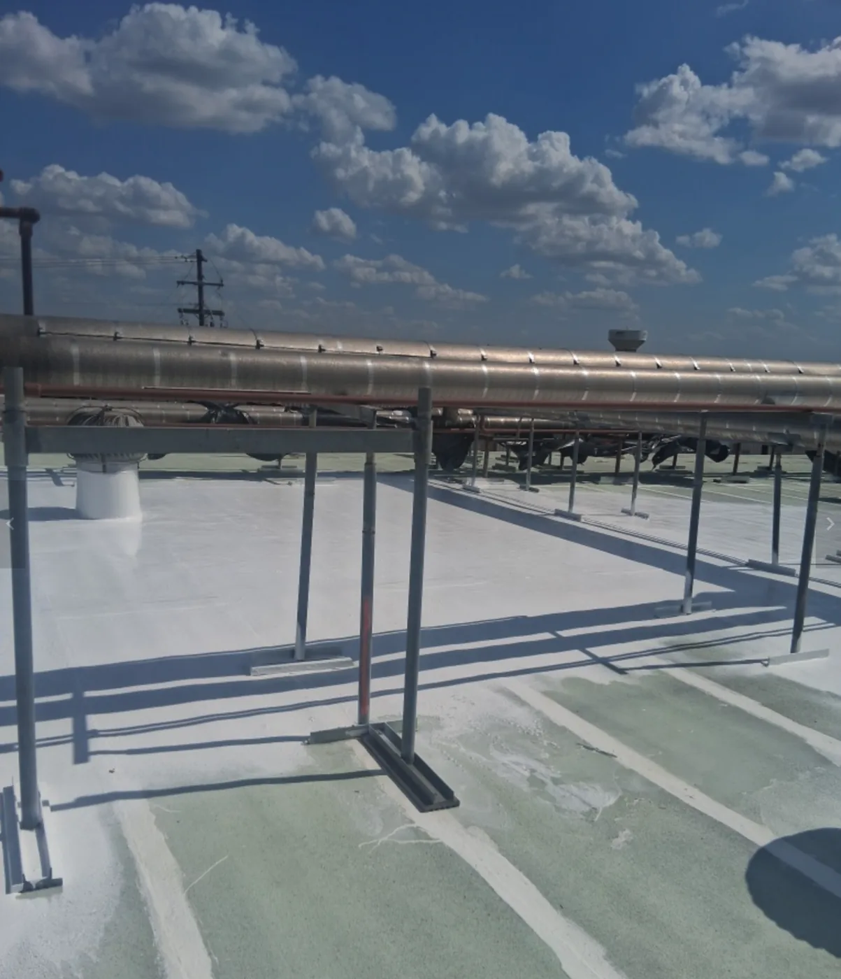Restored white roof surface under a rooftop pipe rack