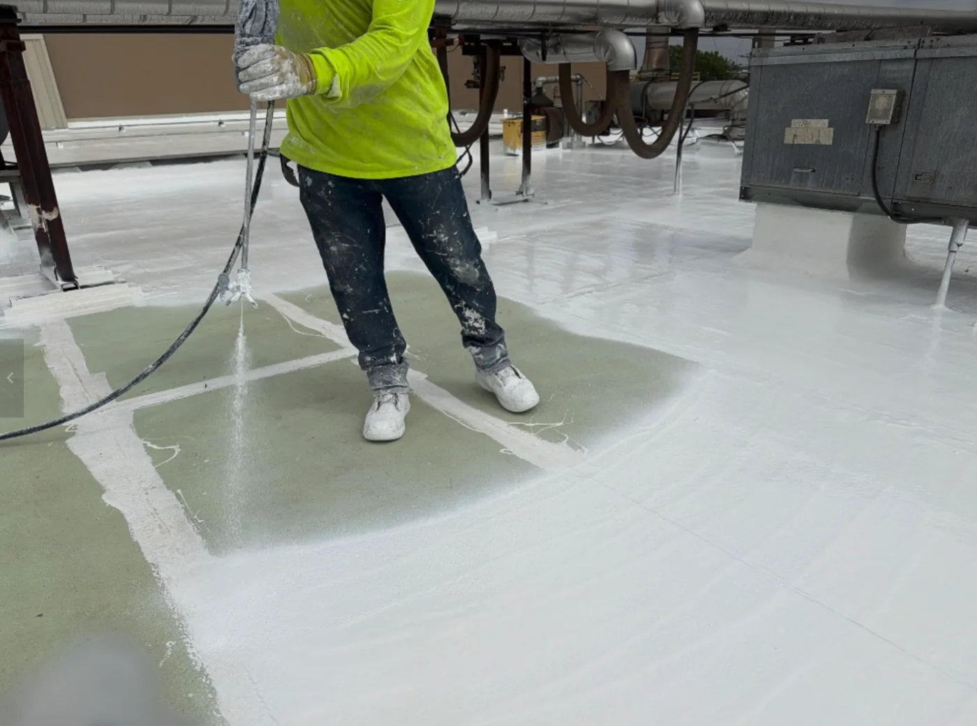 Ramtech crew member spray-applying primer across a large commercial roof