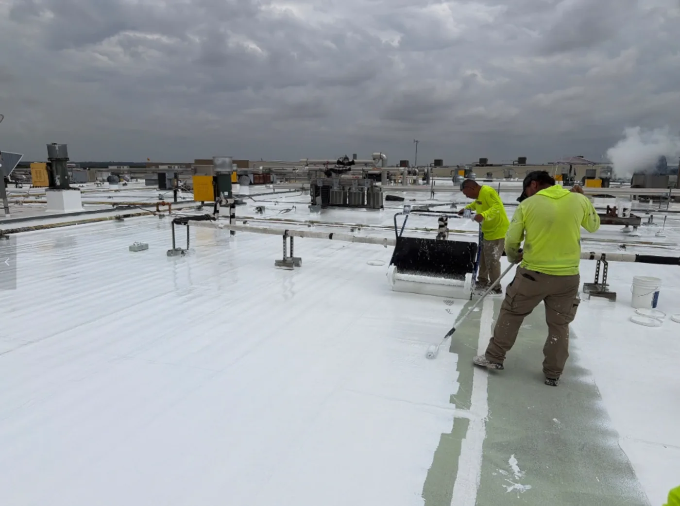Two Ramtech crew members rolling the restoration layer on a white commercial roof