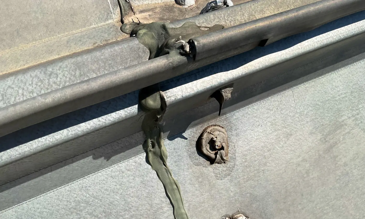 Backed-out fasteners and old sealant on a metal roof rib