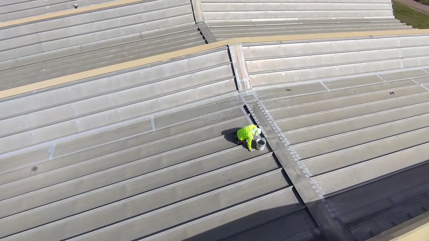 Roofer working along the seams of a long metal roof section