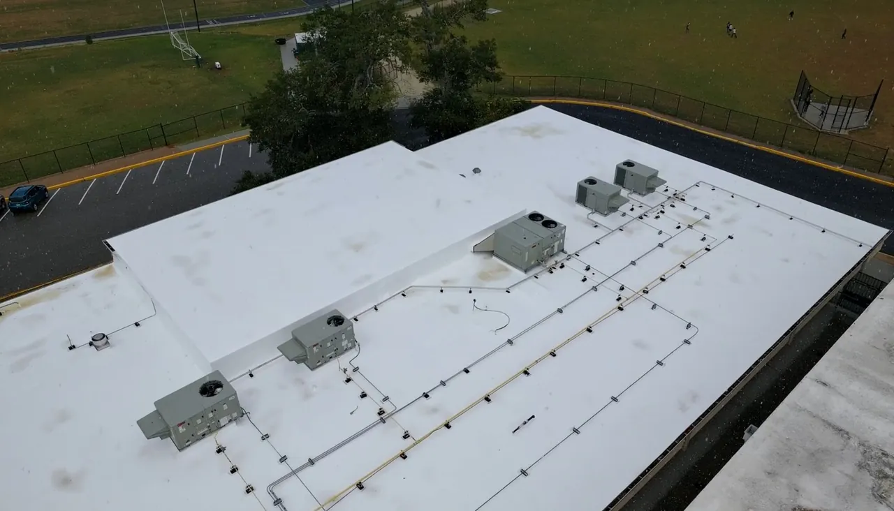 Aerial view of a restored white school roof with rooftop units and conduit runs